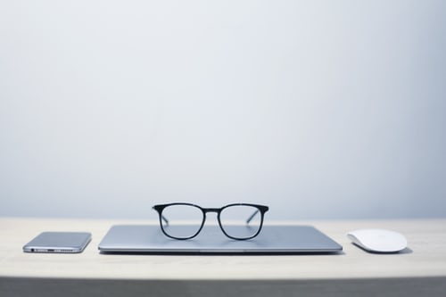 CLosed laptop on desk with reading glasses resting on top